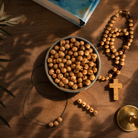 Wooden beads in a bowl with a rosary and bible on a brown surface