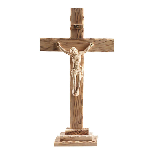 The 'Divine Presence' Olive Wood Crucifix, with a detailed three-dimensional figure of Christ and the inscription 'INRI' above His head. The crucifix features a natural wood grain finish and comes with a removable stand for versatile display options. Handcrafted by Christian families in the Holy Land, it embodies spiritual artistry and heritage.