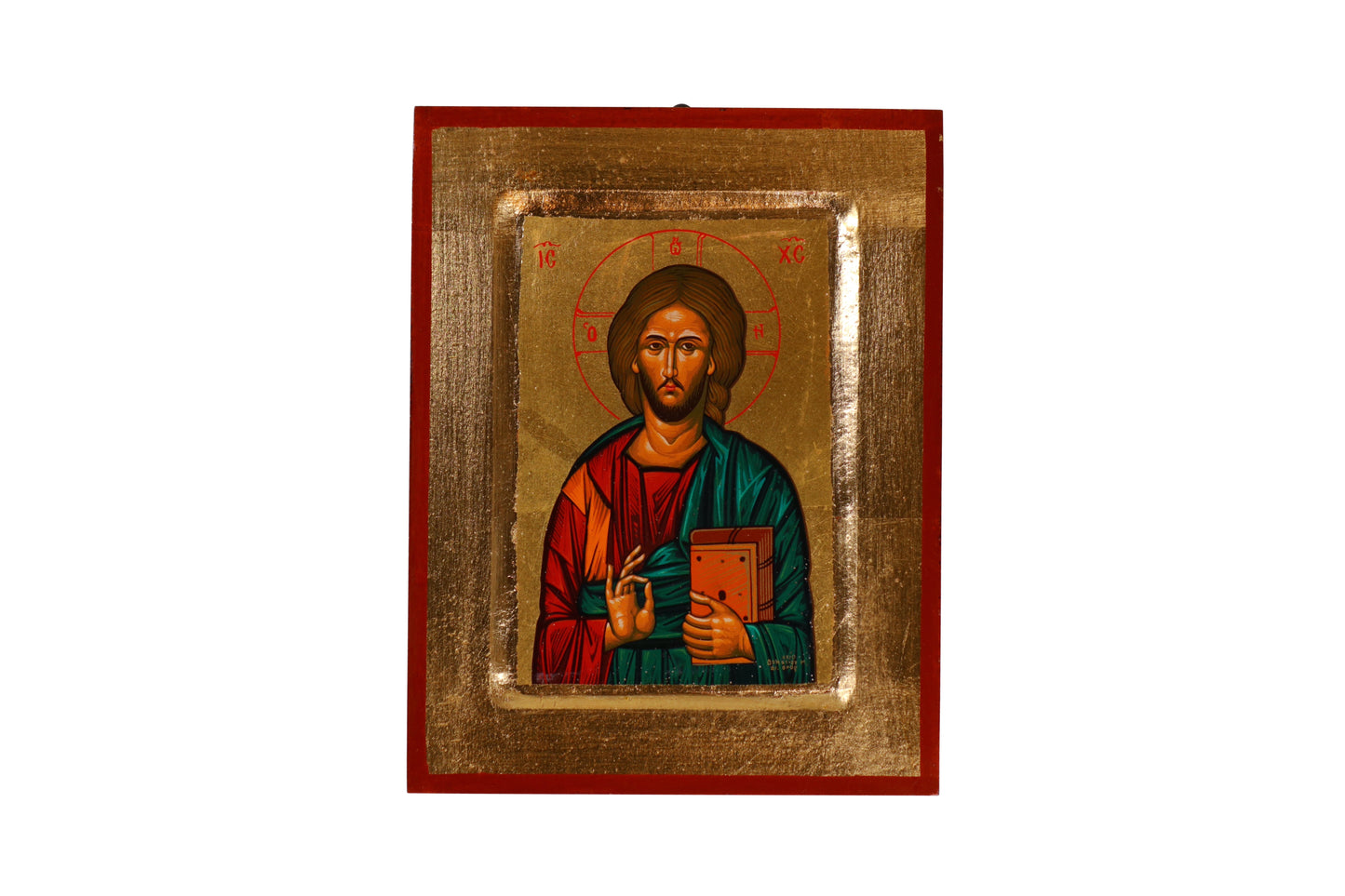 An Eastern Orthodox icon of Jesus Christ centered within a red frame, featuring Christ with a solemn expression, haloed head, blessing with His right hand, and holding an open book in His left. The halo bears the Greek letters "IC XC," and He is robed in red and green with golden highlights, set against a golden background.