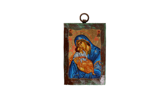 An icon of the Virgin Mary in a blue robe holding the child Jesus, with both figures haloed against a gold leaf background. Above them are two angels, and the icon is bordered by a dark, textured frame with a metal loop at the top for hanging.