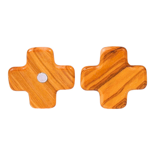 A single olive wood cross-shaped magnet is displayed in two views side-by-side. On the left, the front view shows the warm, striated tones of the polished wood with a central metal magnet visible. On the right, the back view highlights the magnet's housing within the wood, showcasing the natural grain patterns. The cross has rounded edges and is not paired with another piece.