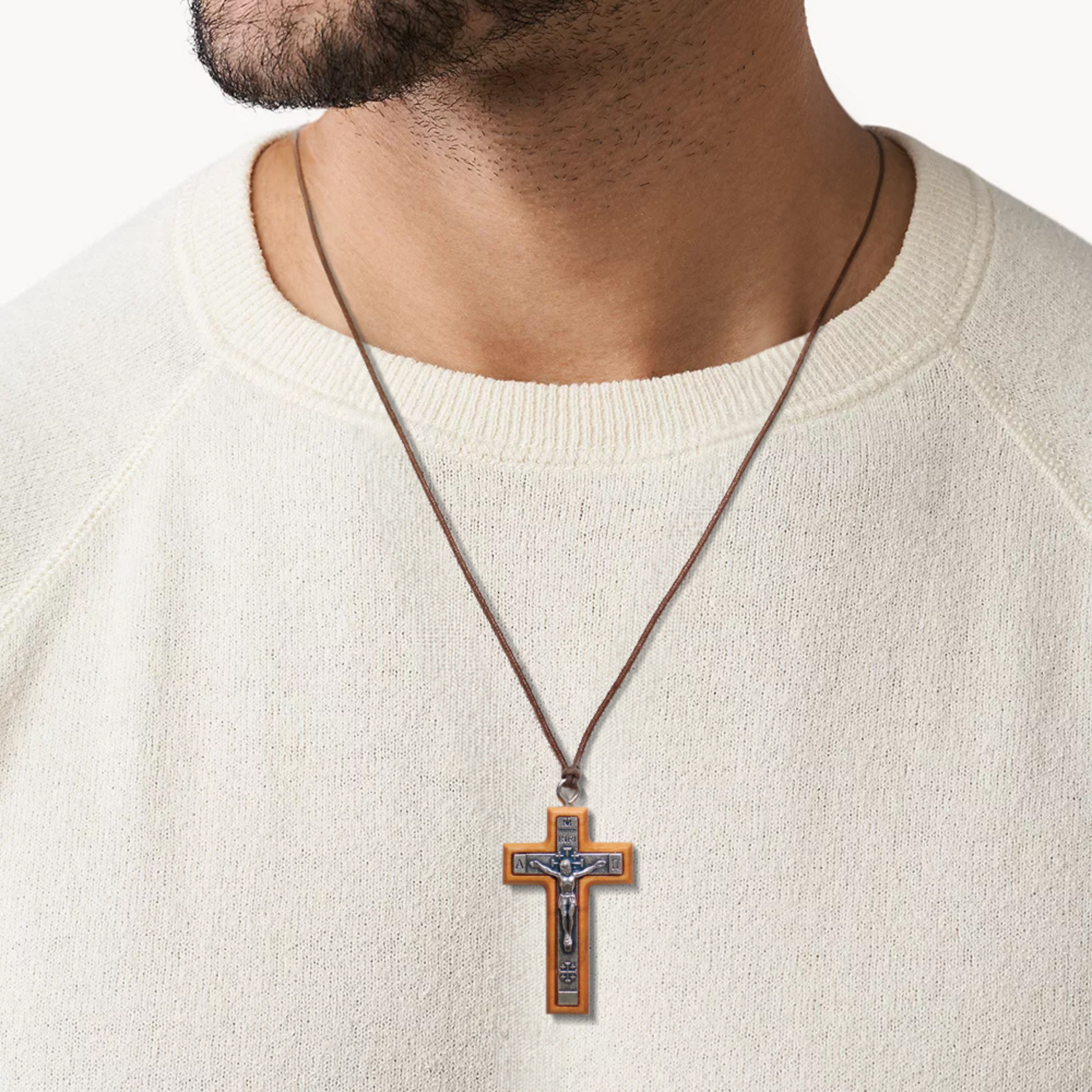 Man wearing a white sweater with a cross pendant necklace on a plain background
