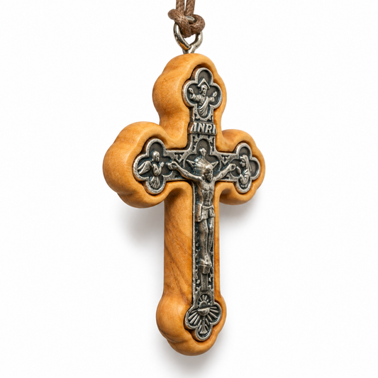 A wooden and metal crucifix pendant necklace on a white background. The cross features a light brown olive wood frame with a silver-toned metal center depicting Jesus Christ on the cross, with an INRI plaque at the top and a brown cord loop at the very top. At an Angle