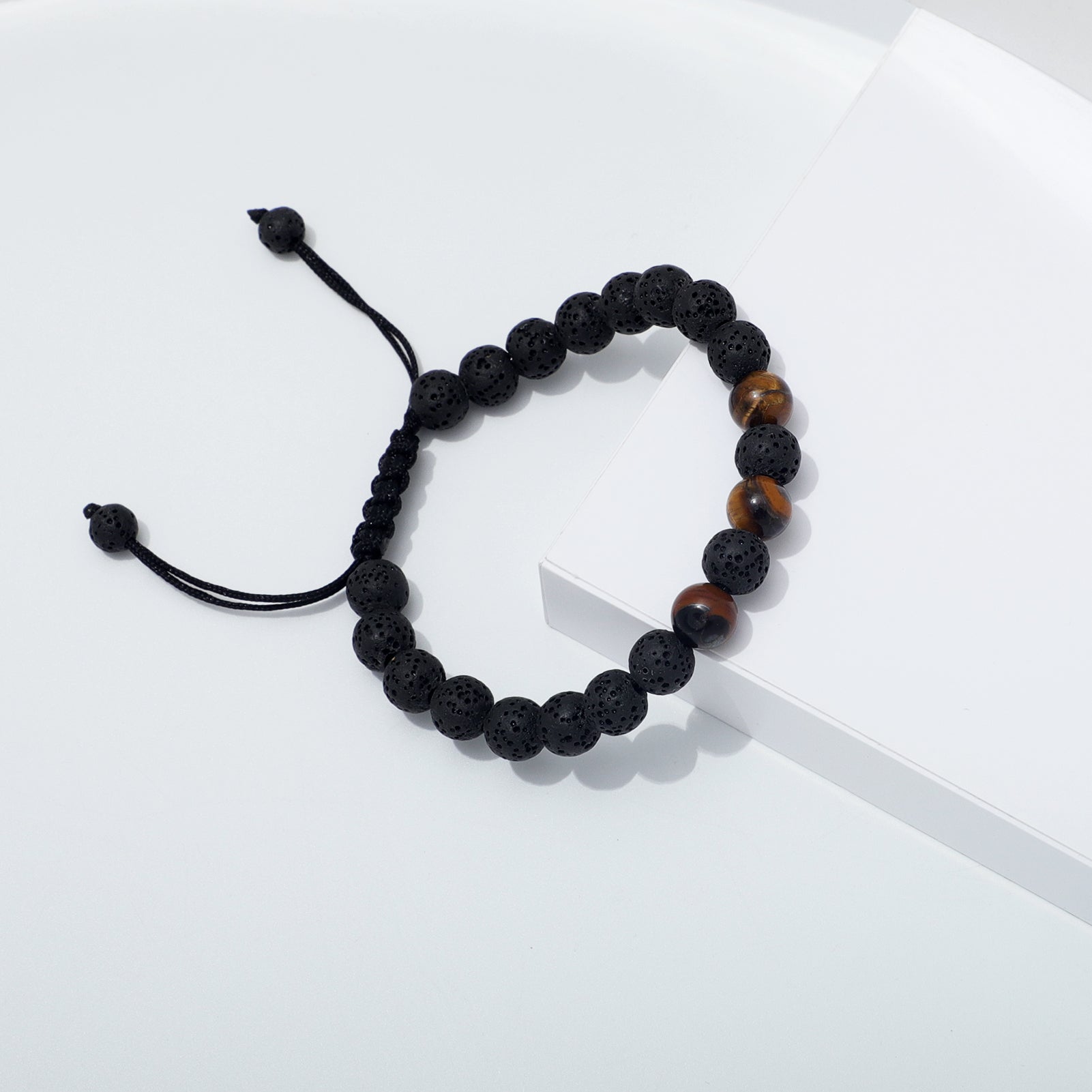 Side Angle of Tiger Eye and Lava Stone Bracelet Draped Over White Edge