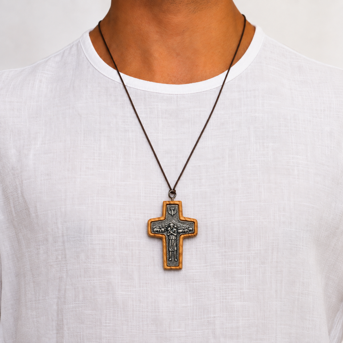 Man in a white shirt wearing the large Good Shepherd olive wood cross necklace with silver toned detail on a brown cord.