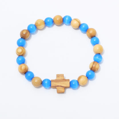 A beaded stretch bracelet featuring alternating bright blue and natural light brown wooden beads, completed with a small wooden cross charm at the front, set against a plain white background.