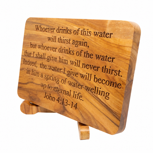 A rectangular wooden plaque with rounded corners and a small matching wooden easel stand, engraved with the Bible verse John 4:13-14. The plaque is made of olive wood with a warm honey-brown grain pattern, photographed on a clean white background.