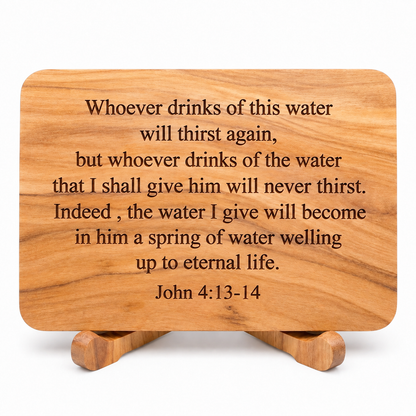 A rectangular wooden plaque with rounded corners and a small matching wooden stand, engraved with the John 4:13-14 Bible verse. The plaque is shown on a clean white background.