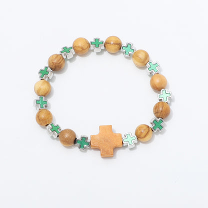 A beaded stretch bracelet featuring light brown wooden beads, small green cross charms with silver edges, and a larger central wooden cross, displayed on a clean white background.
