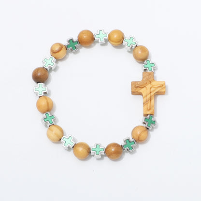 A wooden rosary-style beaded bracelet with light brown olive wood beads, a wooden crucifix, and small mint green cross charms set in silver, displayed on a clean white background.