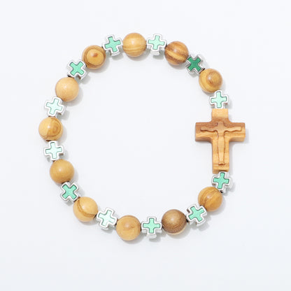 A wooden beaded bracelet featuring light brown olive wood beads, a carved wooden crucifix, and mint green enamel cross charms outlined in silver, displayed on a clean white background.