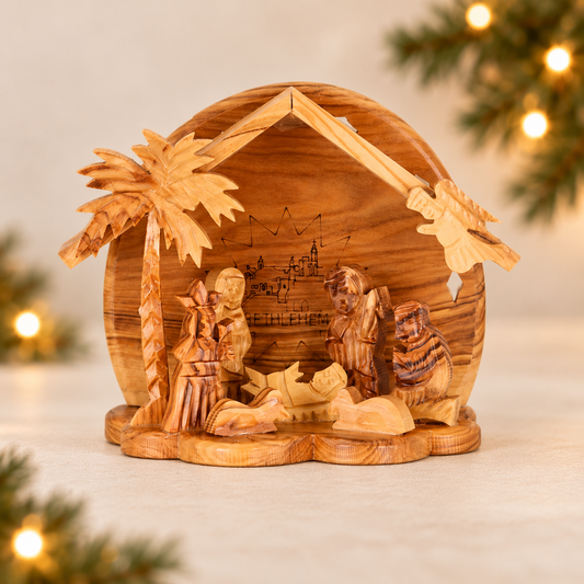 Hand-carved olive wood nativity scene with a thatched-roof stable, palm tree, and small wooden figures
