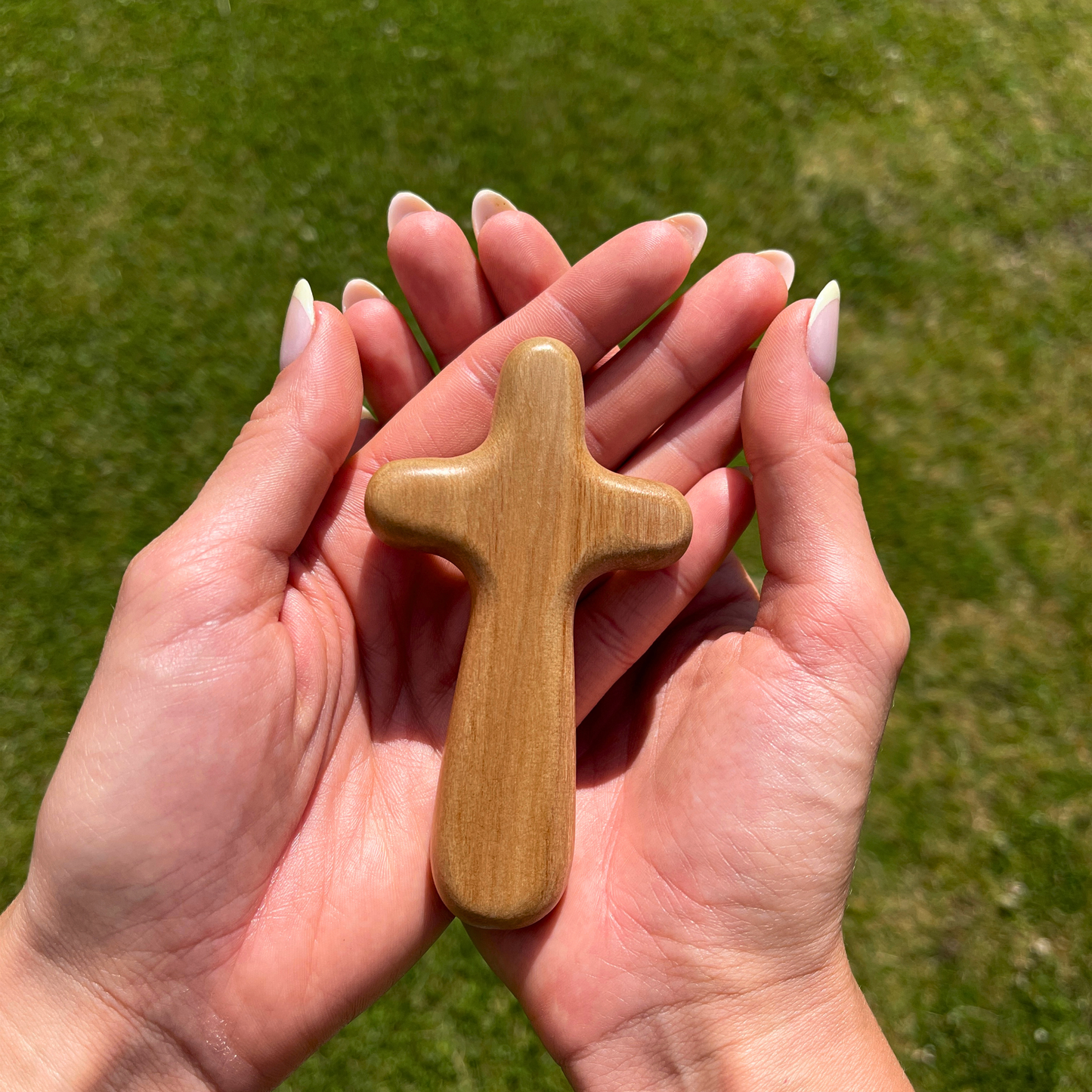 Wooden cross held in hands against a grassy background