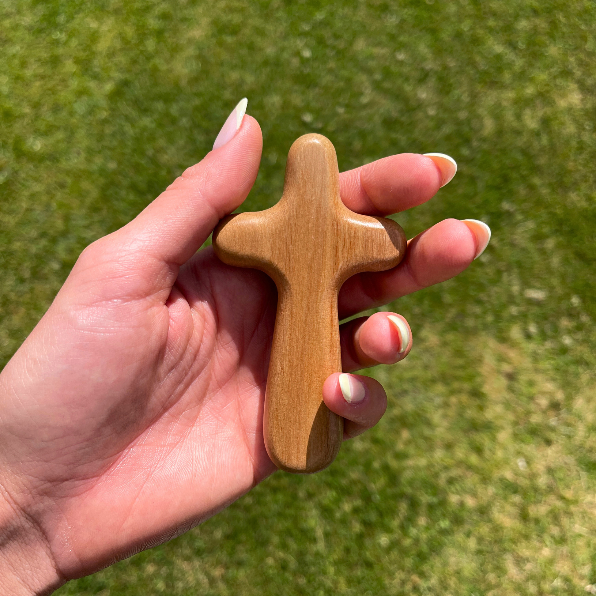 Hand holding a wooden cross against a grassy background