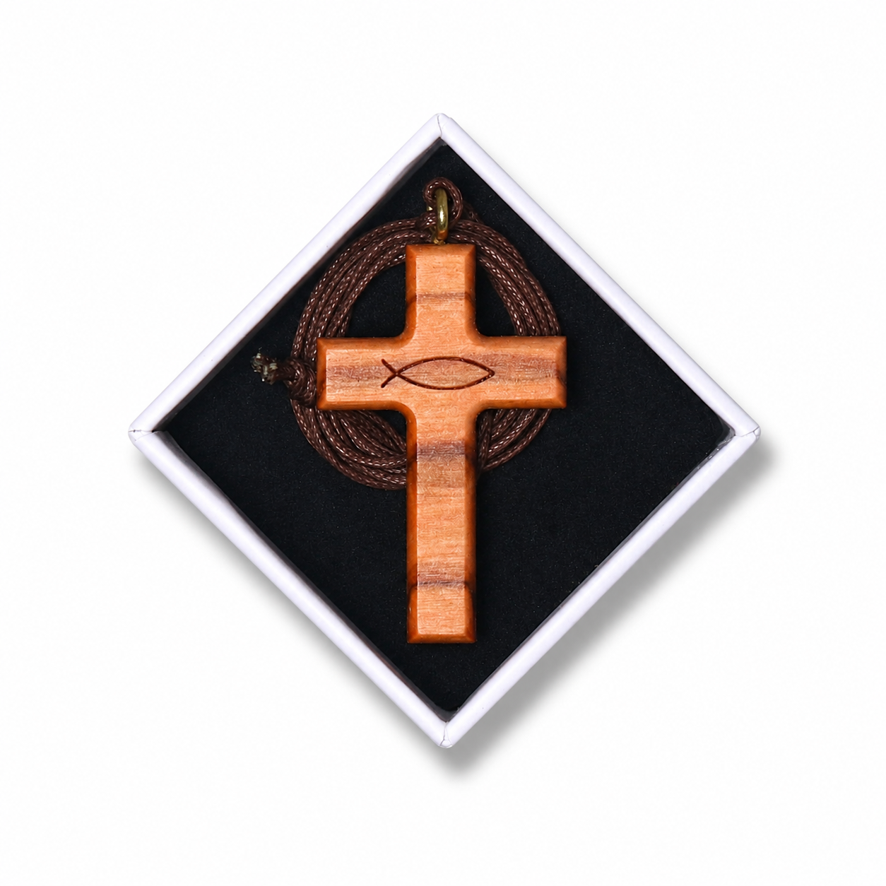 A wooden cross pendant with an engraved fish symbol, displayed inside a black presentation box with a white diamond-shaped border. A brown cord is wrapped around the cross.