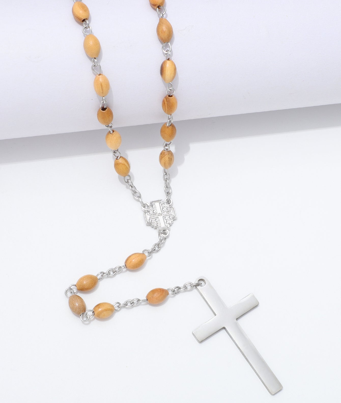 A rosary necklace with light brown wooden beads, silver-tone chain links, a silver centerpiece, and a polished silver cross, displayed on a clean white background.