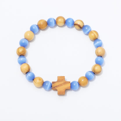 A beaded stretch bracelet featuring alternating light blue and natural wood beads, with a small wooden cross charm at the front, displayed on a clean white background.