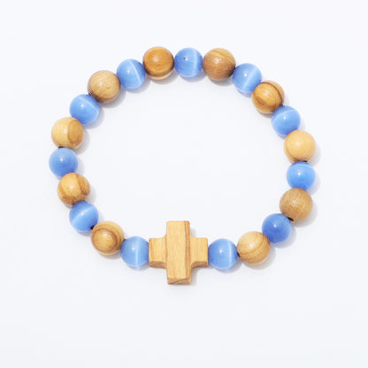 A beaded stretch bracelet featuring alternating light blue and natural wood beads, finished with a central wooden cross charm, shown on a plain white background.