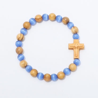 A beaded rosary-style bracelet featuring alternating light blue and natural wood beads, with a small wooden crucifix at the end, displayed on a clean white background.
