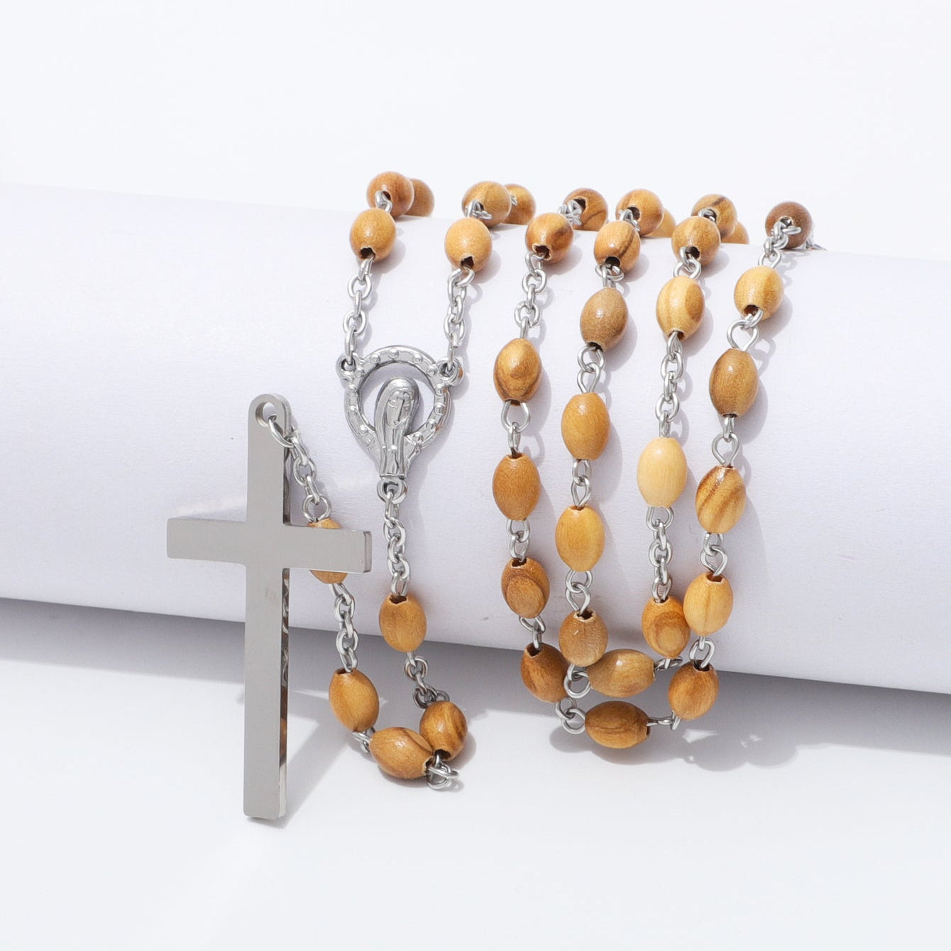 A rosary-style necklace with light brown wooden beads and silver-tone metal links, chain, centerpiece, and cross pendant, displayed on a white cylindrical prop against a white background.