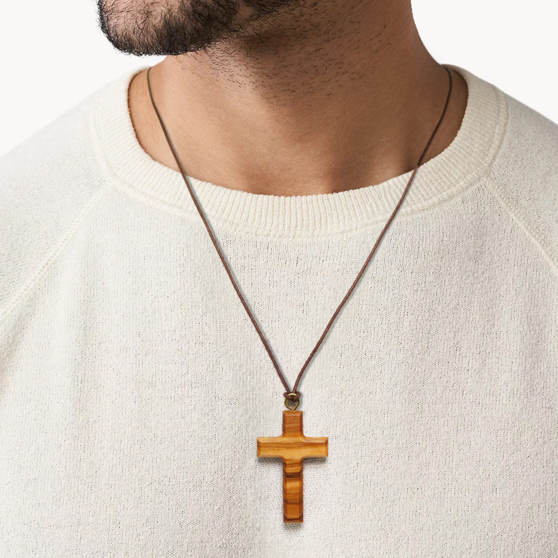 Man wearing a white sweater with an olive wood cross necklace.
