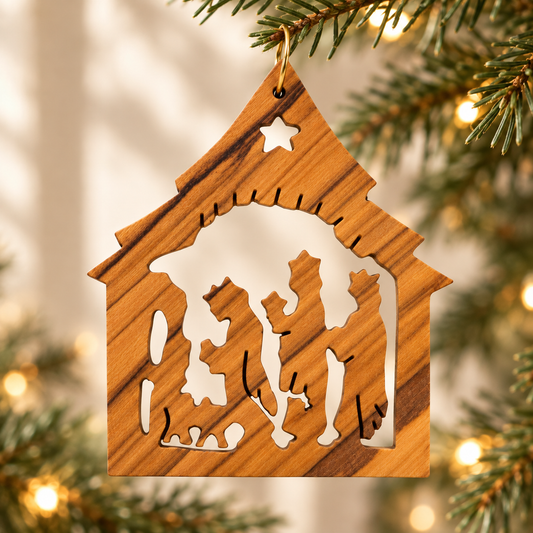 A wooden nativity ornament with a warm brown wood-grain finish, hanging from a green Christmas tree branch with warm bokeh lights in the background.