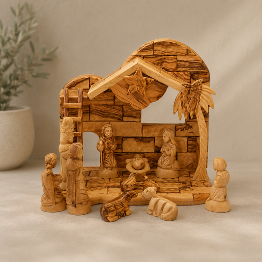 Hand-carved olive wood nativity scene with multiple figures and a stable structure, displayed on a neutral fabric surface with a soft-focus plant in the background.