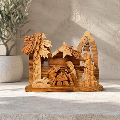 Hand-carved olive wood nativity scene figurine displayed on a light stone surface with a blurred potted plant in the background.