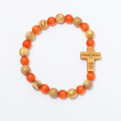A beaded bracelet featuring alternating round orange beads and natural light wood beads, with a small carved wooden cross at the front, photographed on a clean white background.