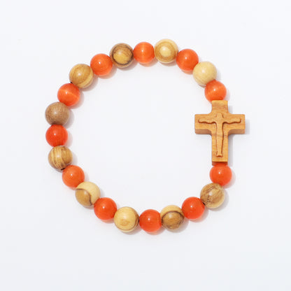 A beaded rosary-style bracelet with alternating orange and natural wood beads, featuring a carved wooden cross charm, photographed on a clean white background.