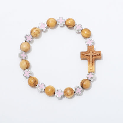 A wooden bead bracelet featuring natural olive wood beads, light pink enamel cross charms, and a larger wooden crucifix pendant, displayed on a clean white background.