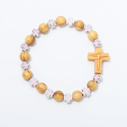 A wooden bead bracelet featuring natural wood beads, light pink enamel cross charms, silver-toned spacer details, and a carved wooden cross pendant, displayed on a clean white background.
