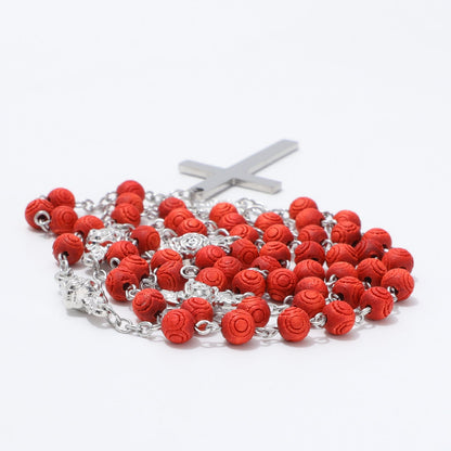 A rosary with red rose-shaped beads and a silver-tone metal crucifix, photographed on a clean white background.