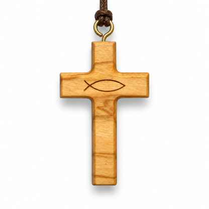 A light-colored olive wood cross pendant featuring an engraved Christian fish symbol at the center, suspended from a dark brown cord with a brass ring, shown against a plain white background.