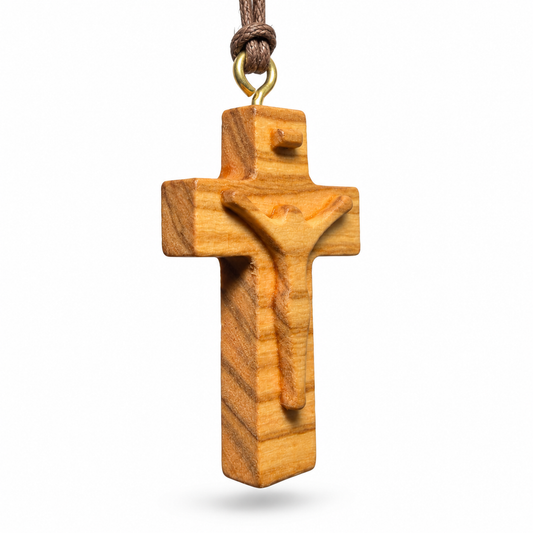 A wooden crucifix pendant with a carved figure of Jesus Christ, suspended from a brown cord with a gold-colored metal ring, shown against a plain white background.