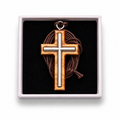 A wooden cross pendant with a silver-toned center and a brown braided cord, presented inside a square white gift box with a black insert.
