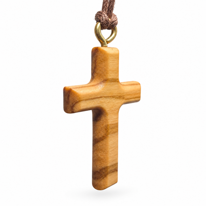 A small wooden cross pendant with a natural light brown grain pattern, hanging from a brown cord with a gold-colored metal loop, shown against a plain white background.