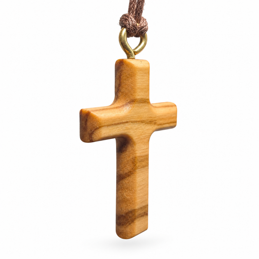 A small wooden cross pendant with a natural light brown grain pattern, hanging from a brown cord with a gold-colored metal loop, shown against a plain white background.