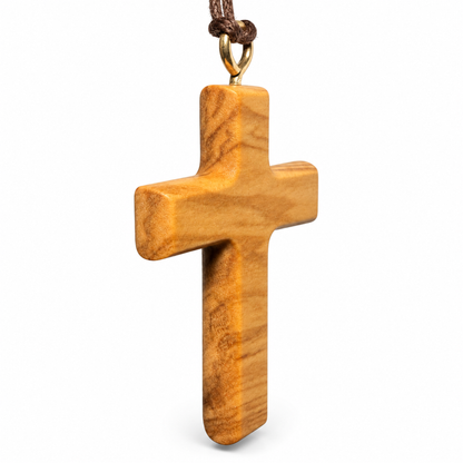 A wooden cross pendant with a natural olive wood grain pattern, hanging from a brown cord with a gold-colored metal loop, shown against a plain white background.