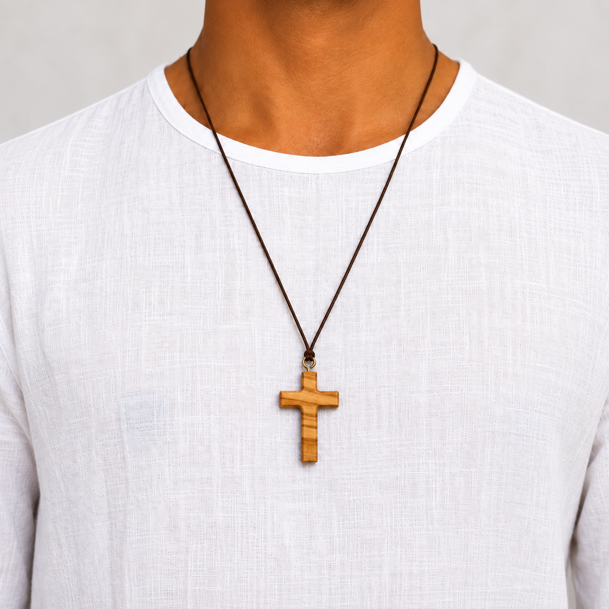 A close-up of a person wearing a wooden cross pendant necklace on a dark cord over a white linen shirt.