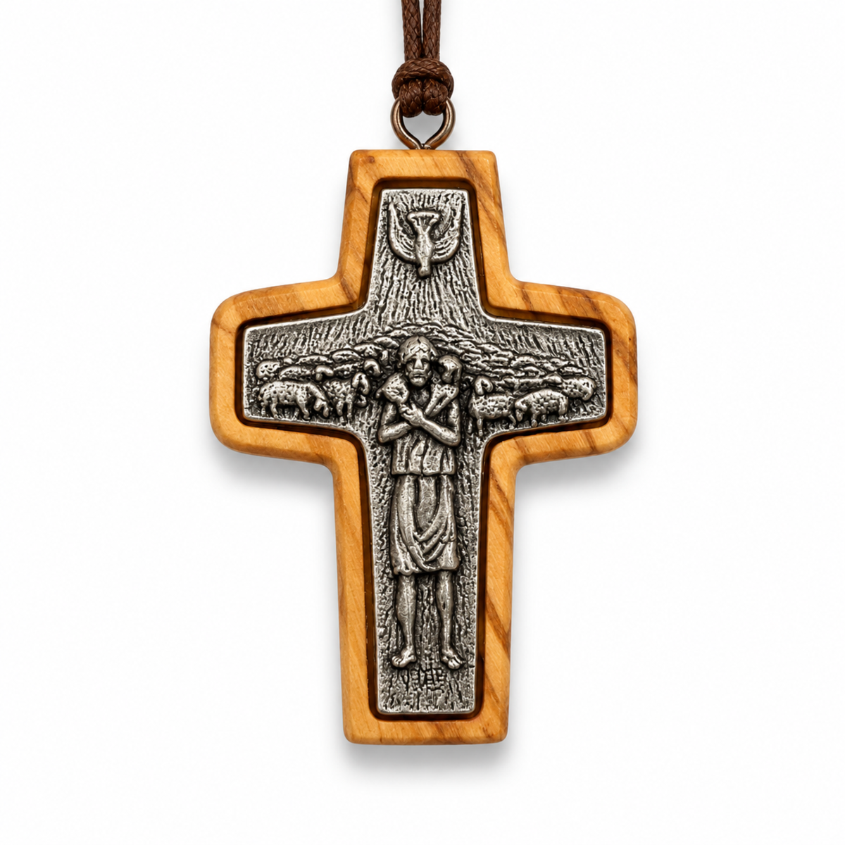 A wooden cross pendant with an olive wood grain finish and a detailed silver-toned metal centerpiece depicting Jesus and sheep, suspended by a brown cord on a white background.