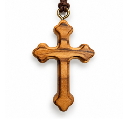 A wooden Orthodox cross pendant with a natural olive wood grain pattern, hanging from a dark brown cord with a brass ring, shown against a plain white background.