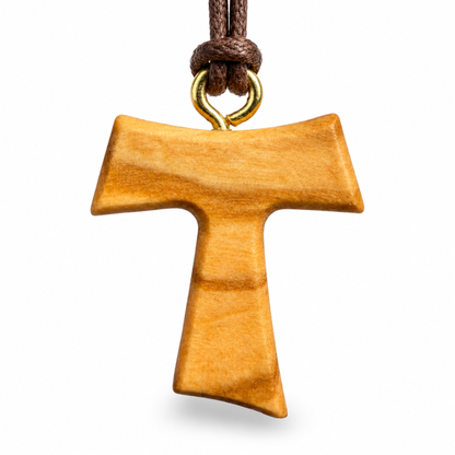 A wooden T-shaped pendant with a natural warm brown finish, suspended from a dark brown cord with a gold-colored metal loop, shown against a plain white background.