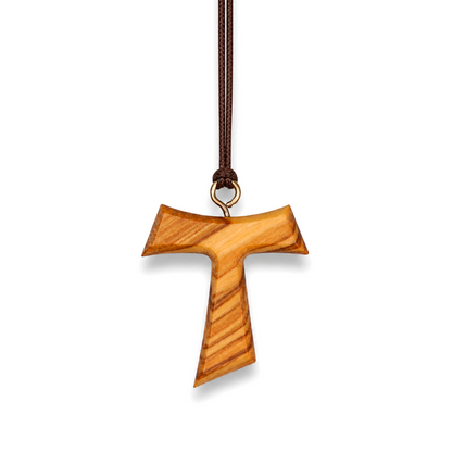 A wooden cross pendant with a natural olive wood grain pattern, suspended from a dark brown cord with a small gold-colored metal ring at the top, set against a plain white background.