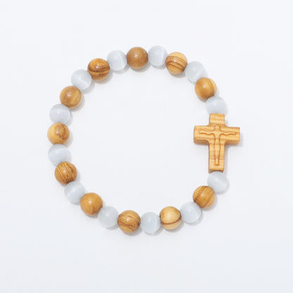 A beaded stretch bracelet featuring light brown wooden beads, translucent white cat's eye beads, and a carved wooden crucifix, displayed on a clean white background.