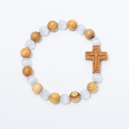 A beaded rosary-style bracelet with alternating light brown wood beads and translucent white beads, featuring a carved wooden cross on a plain white background.