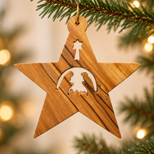 A wooden star Christmas ornament with a nativity scene cutout hangs from a pine tree branch with warm bokeh lights in the background.