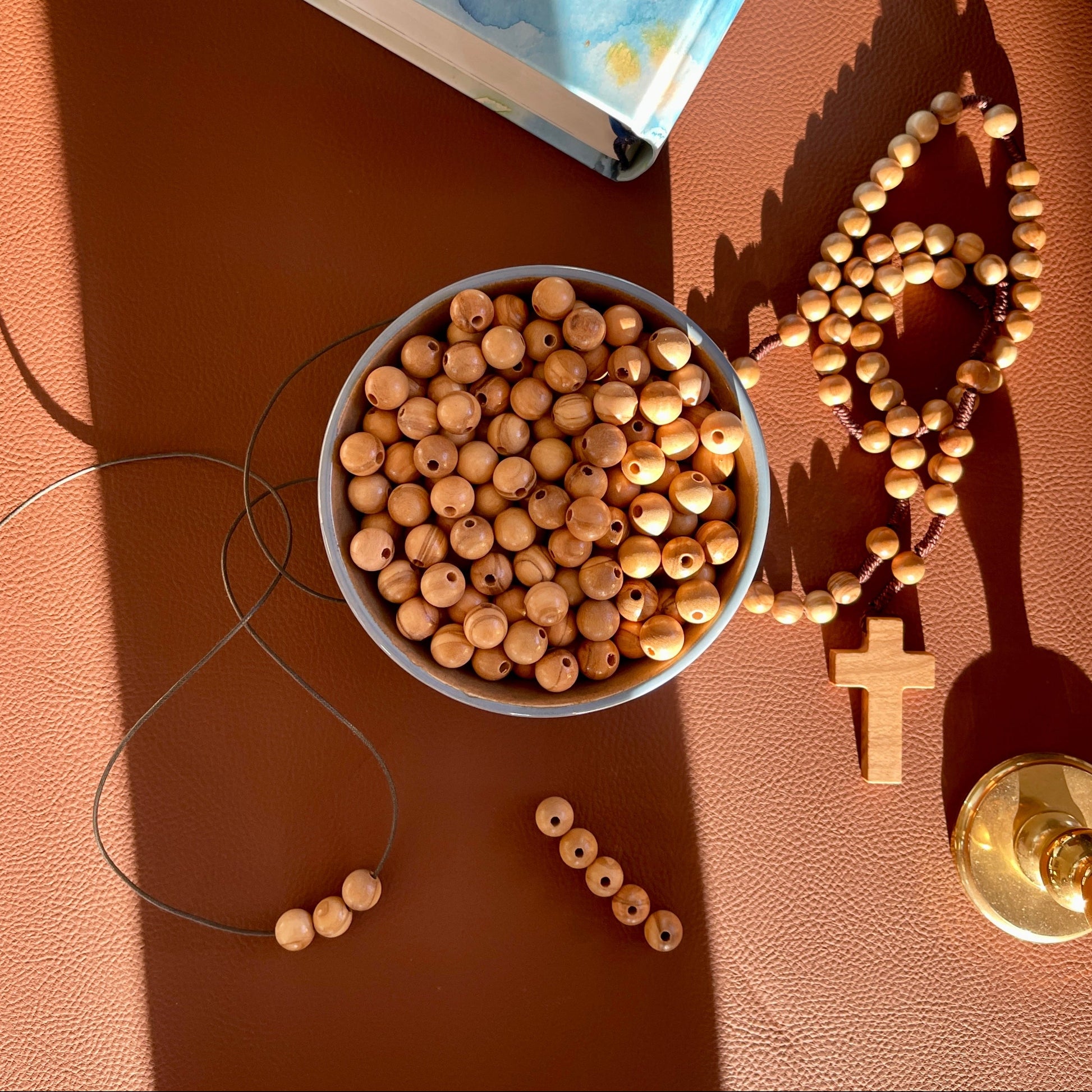Wooden beads in a bowl with a rosary and book on a brown surface