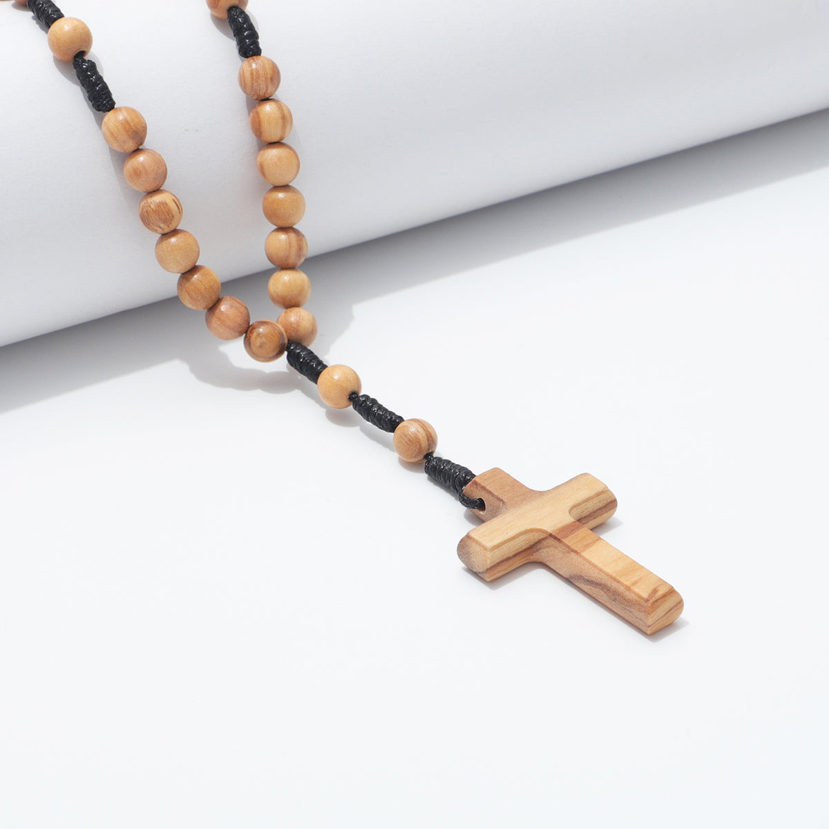 Detail of 6mm olive wood beads and black cord draped over a white block beside the cross