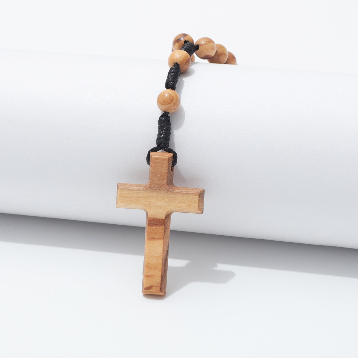 Plain olive wood cross hanging over a white block with two prayer beads above